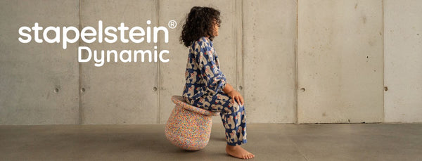 Child balancing on Stapelstein® wobble board and base in playroom.