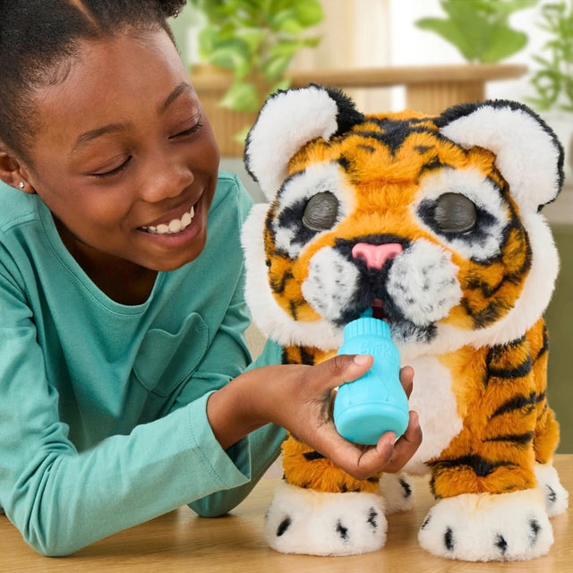 A smiling young girl in a green shirt plays with a plush toy tiger. She holds a small light blue bottle to the toy's mouth.