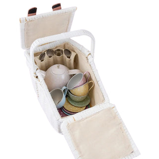A white woven picnic basket with its hinged lid open, showing a pastel-colored tea set inside, including a teapot, cups, saucers, and spoons, on a solid white background.