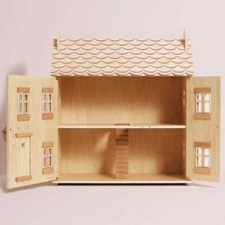 A wooden dollhouse with open doors, showcasing the interior with a painted tile roof, stairs, and small windows, set against a solid pale pink background.