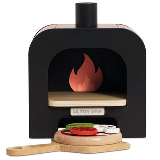 A wooden toy pizza oven set by Le Toy Van, featuring a black oven body with a light wood interior, a flame graphic at the back, and a wooden peel holding a colorful toy pizza with toppings, shown on a white background.