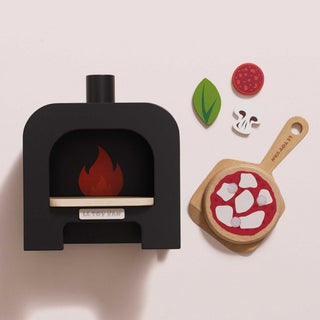 Toy wooden pizza oven with a flame and wooden pizza peel with toppings on a light pink background