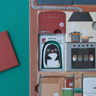 A close-up of a illustrated kitchen with secret compartments, including a hidden penguin figure, amongst cooking pots, cupcakes, and a red drawer labeled Londji, shown on a teal background.