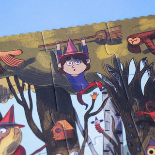 A close-up of a colorful illustrated jigsaw puzzle showing a whimsical forest scene with a child in a witch hat hanging from a flying broom, surrounded by tree trunks, birds, and a house. Puzzle pieces are visible, and the scene fills the frame.