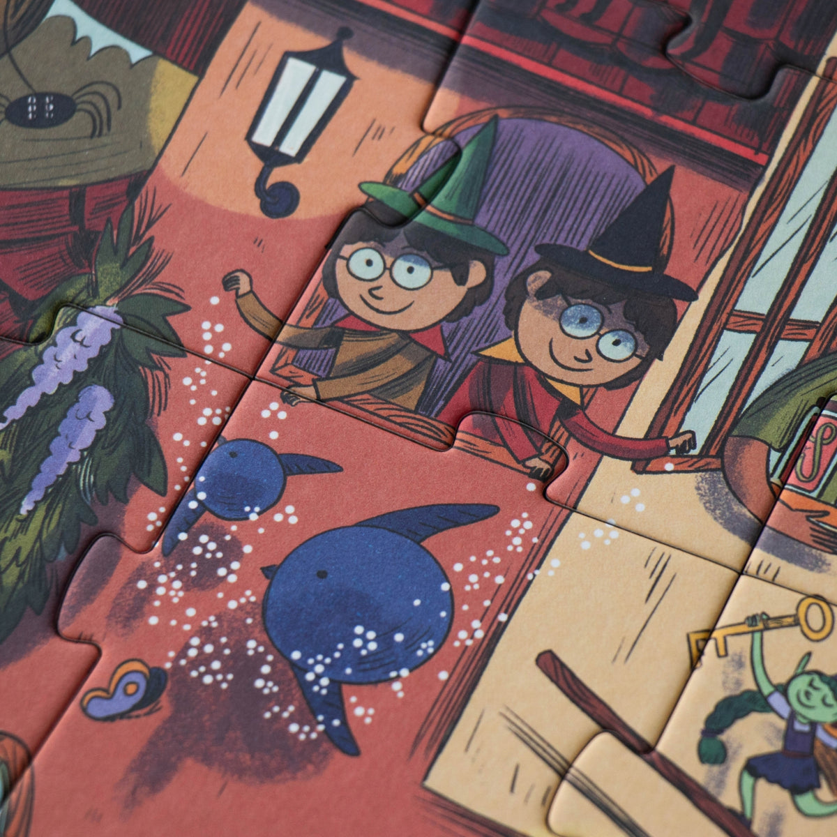 A close-up of a completed jigsaw puzzle showing whimsical illustrated characters and objects, including two children in witch hats, blue birds, a lantern, and a goblin-like fairy figure, with puzzle-piece cutlines visible across the artwork.