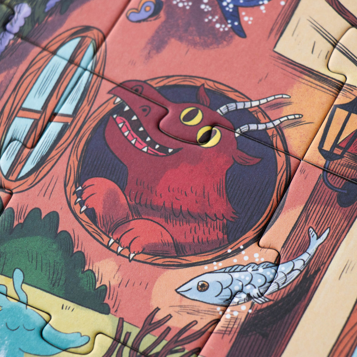 A close-up of a colorful illustrated jigsaw puzzle showing a red monster dragon peeking out of a circular opening, with a fish and fantasy scenery around it.
