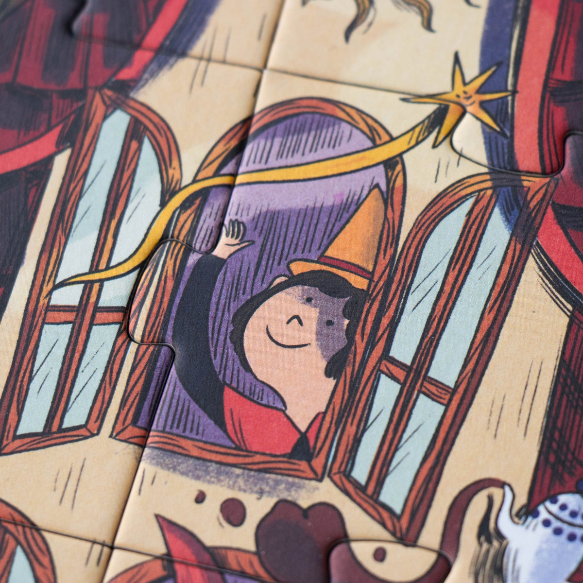 A close-up of a jigsaw puzzle showing a whimsical child with a pointed hat and star wand, set against a warm beige background with red, purple, and blue details.
