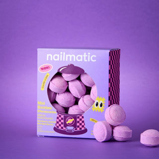 A box of Nailmatic Mini Bath Bombs - Berry Bloom, alongside several loose, round, lavender-colored bath bombs on a matching purple background.