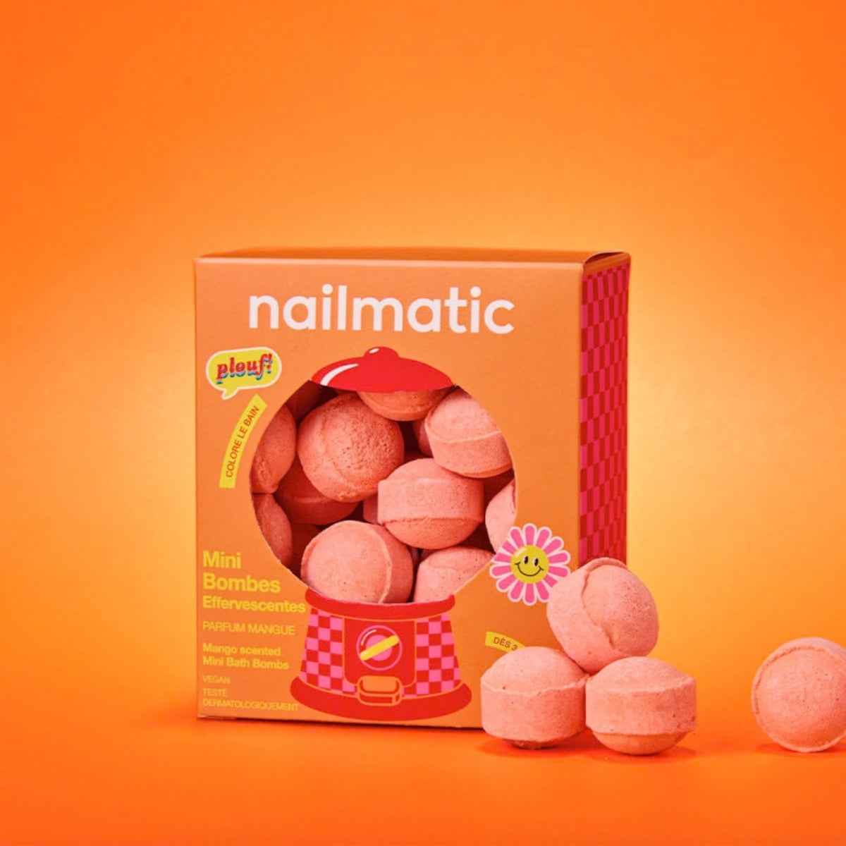 A box of Nailmatic Mini Bombs, shown with several orange round bath bombs spilled in front on a bright orange background.