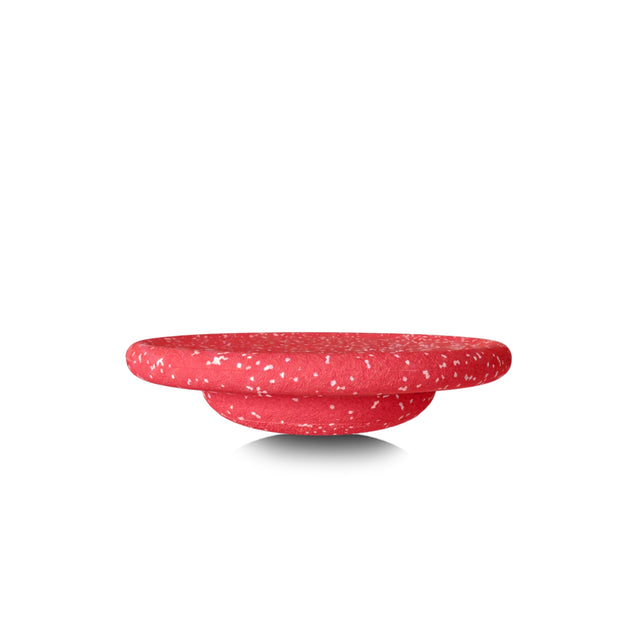 A red speckled round balancing board shown from a side profile view on a white background.