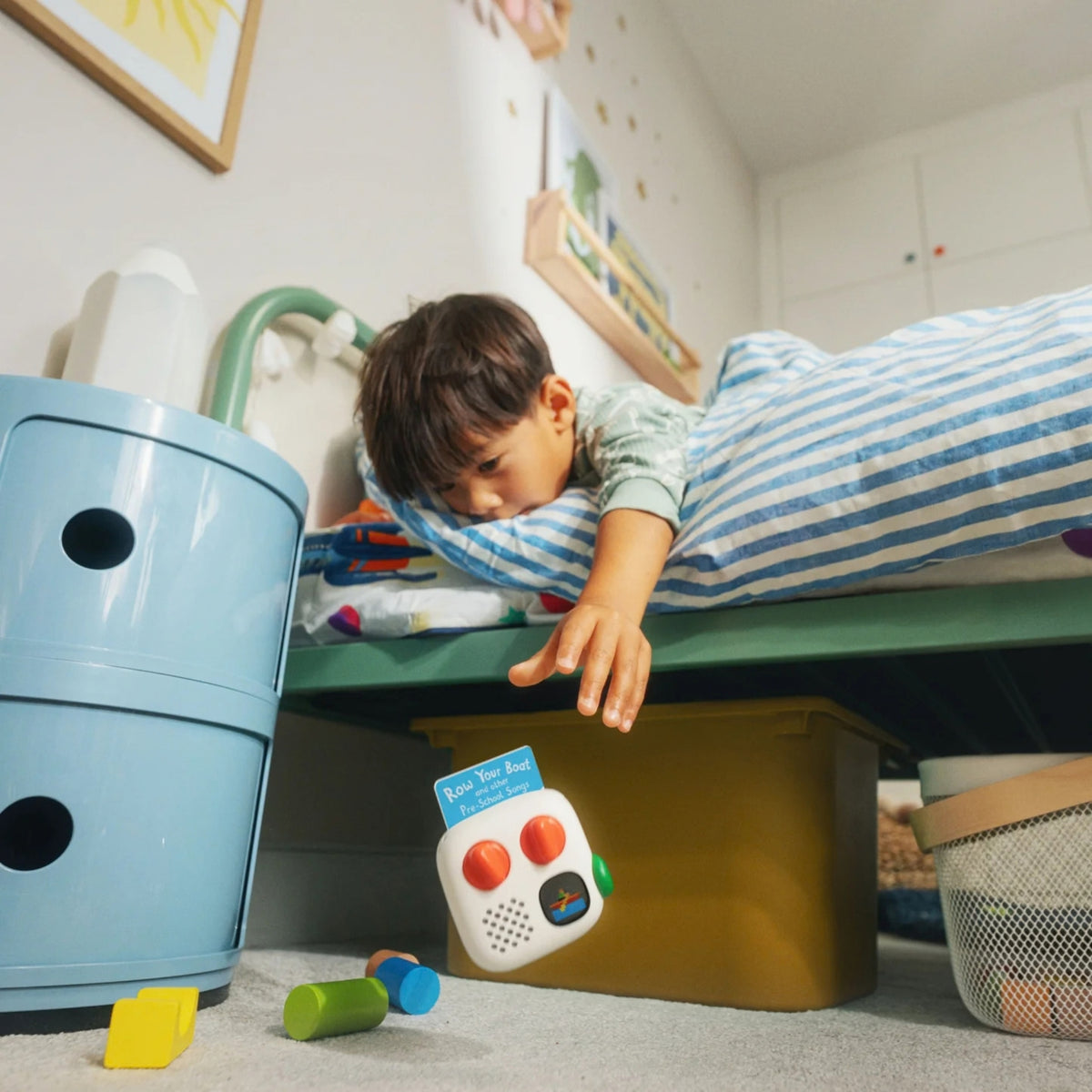 A young boy is leaning out of his bed as his Yoto Mini Palyer 4th Gen has fallen out, it is in mid-air as he grasps for it.