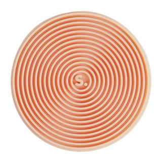 A circular silicone mat with concentric spiral ridges in a peach-orange and cream color scheme, featuring a small 'S' logo in the center for SPEKS.